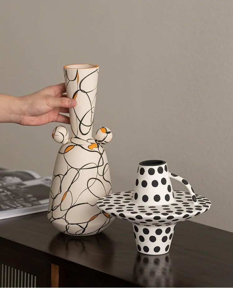 Ceramic vase with abstract design held by a hand on a table.