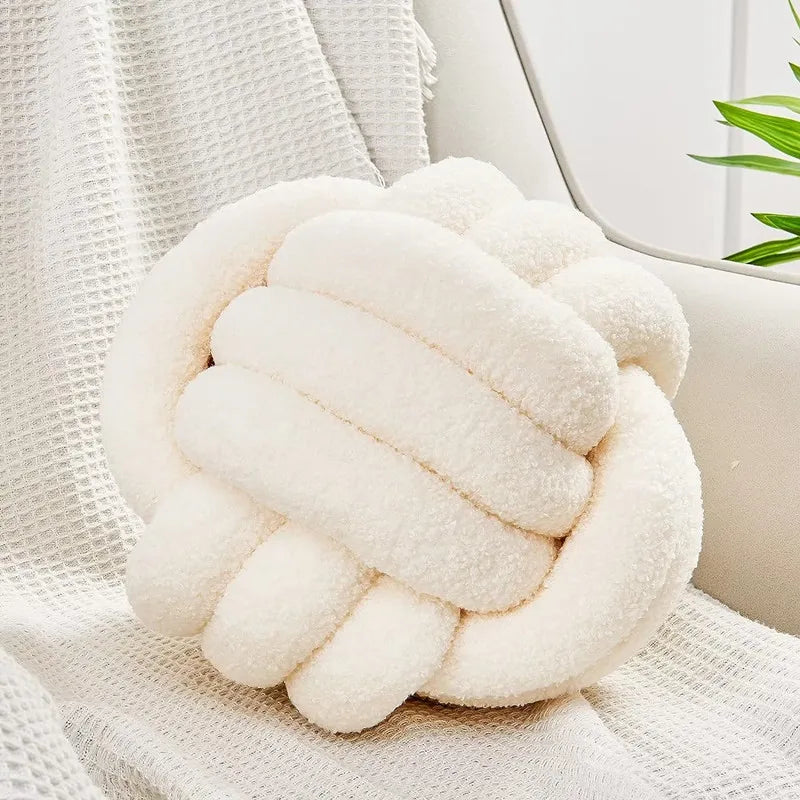 White knot-shaped pillow on a white surface with a neutral background