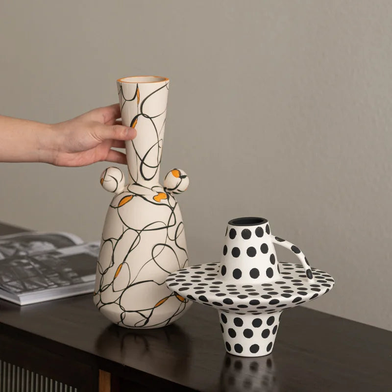 Person holding a ceramic vase with abstract design on a table with another polka dot vase.