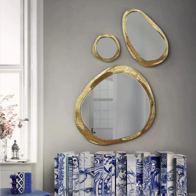 Three gold-framed mirrors of different sizes on a gray wall with decorative books below.
