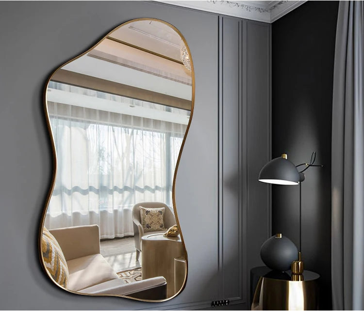 Modern wall mirror with gold frame on a gray wall, reflecting a living room.