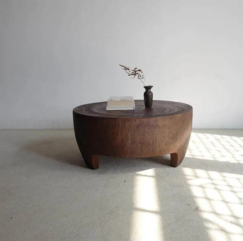 Wooden coffee table with a vase and glass on a light gray floor and white wall.