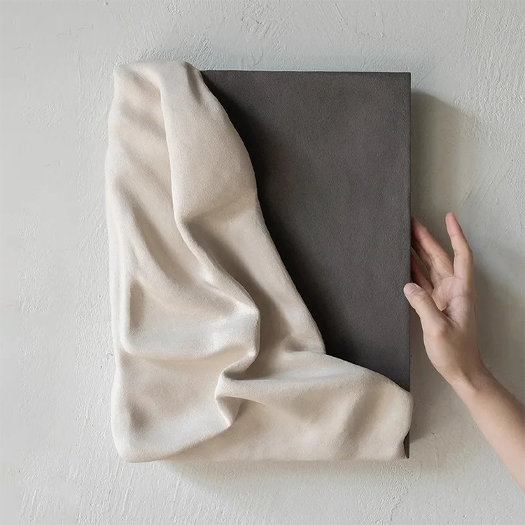 Beige fabric draped over a dark rectangular object against a light gray wall.