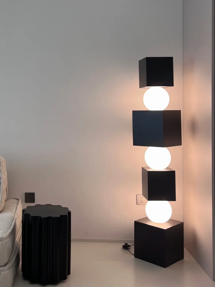 Modern floor lamp with black cube design and white lights in a room setting.