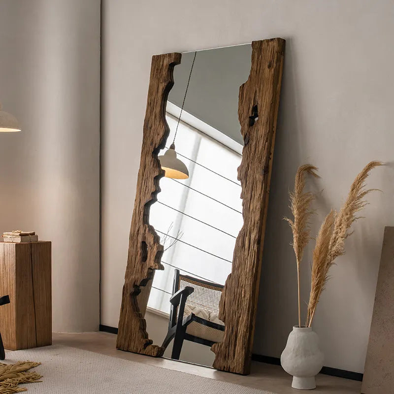 Large wooden-framed mirror leaning against a wall in a room with decor elements.