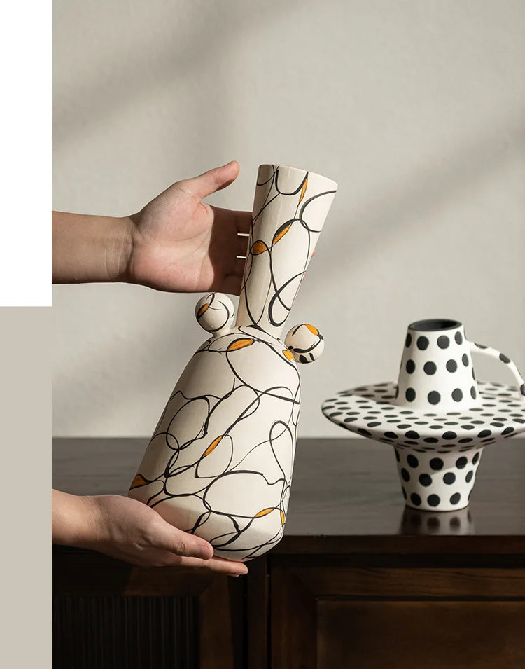 Person holding a decorative vase with abstract patterns, next to a polka dot cup on a table.