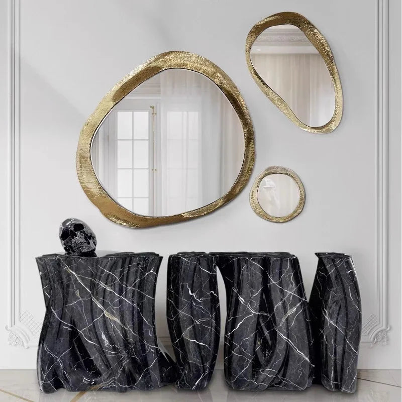 Decorative vases with marble pattern in front of gold-framed mirrors on a white wall.
