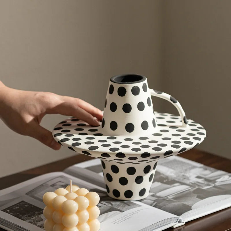 Polka dot ceramic cake stand with a hand holding it, on a table with a magazine underneath.
