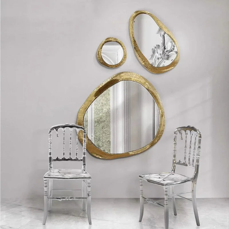 Gold-framed mirrors and clear chairs against a white wall