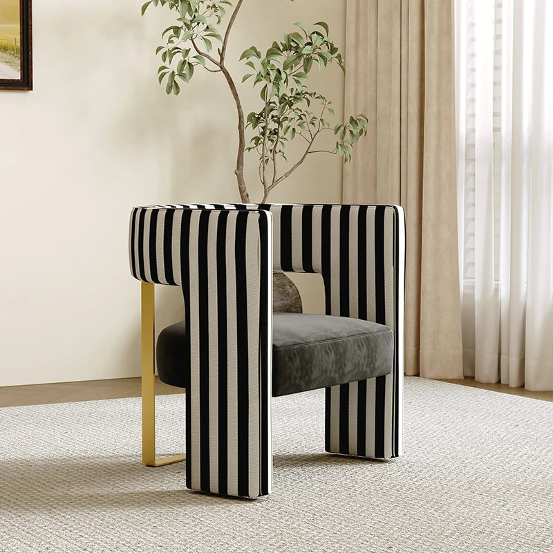 Modern chair with black and white striped legs in a room with a plant and curtains.