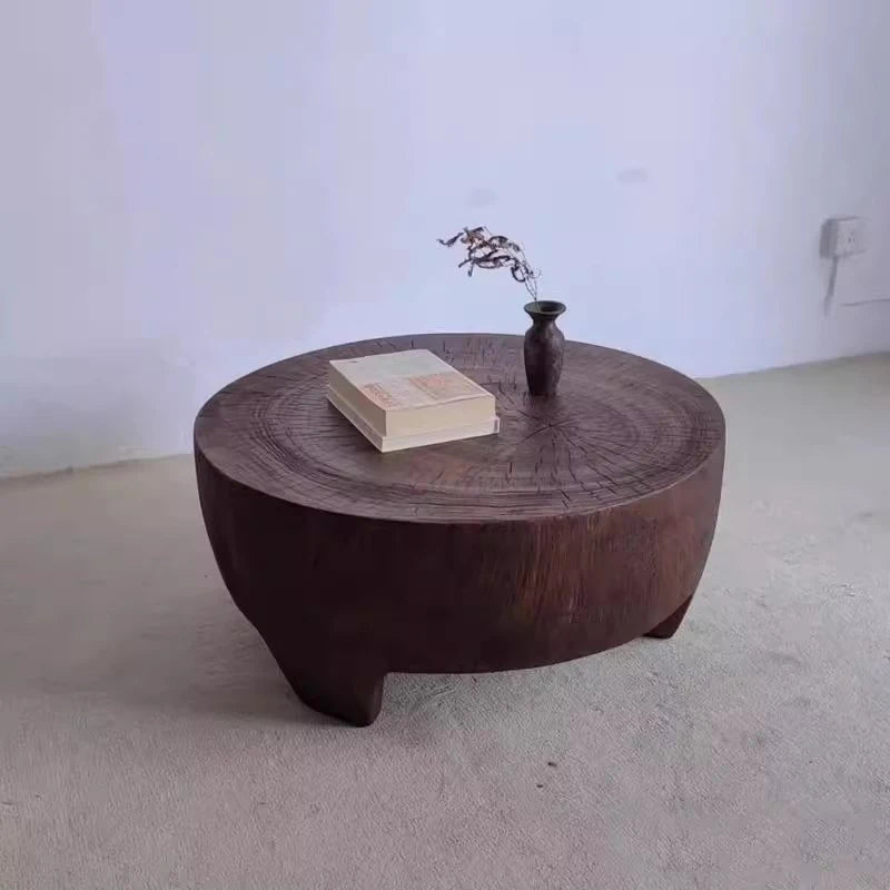 Wooden coffee table with a vase and book on a plain floor.