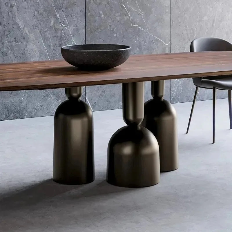 Dining table with wooden surface and bronze metal legs against a gray marble wall.