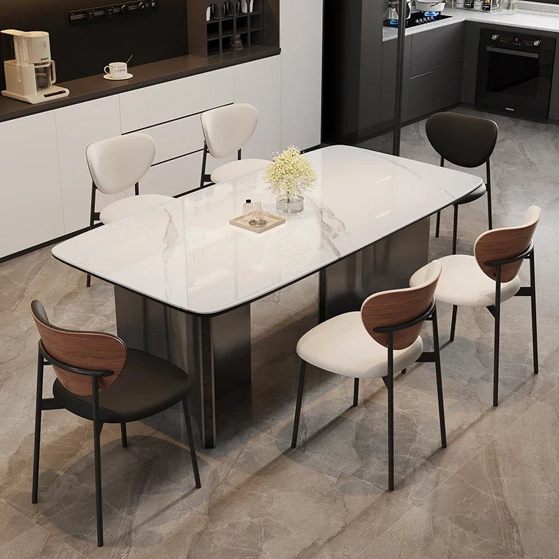 A modern rectangular dining table with a white marble-look top and dark metal base, surrounded by six contemporary chairs with white and wood-look seats and black metal frames, set in a contemporary kitchen interior.