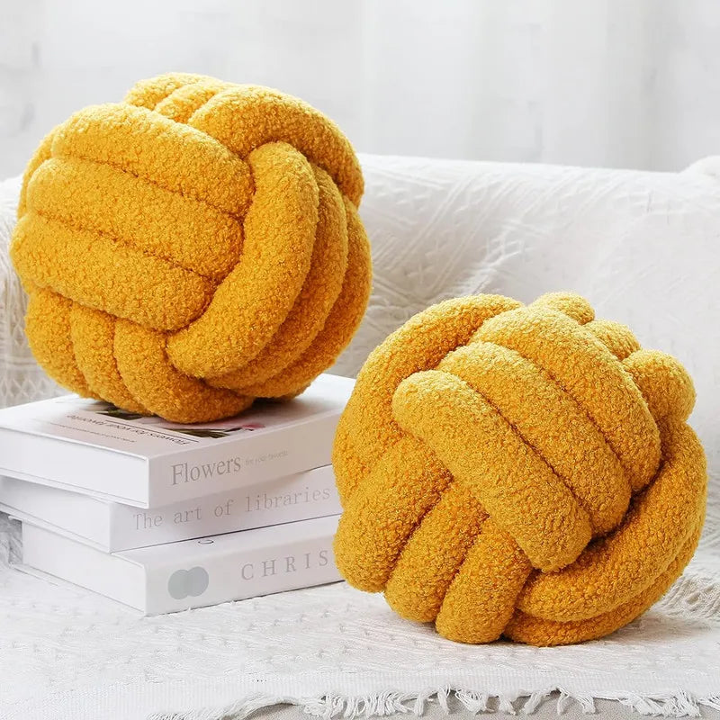 Two yellow knot-shaped cushions on a white surface with books underneath.