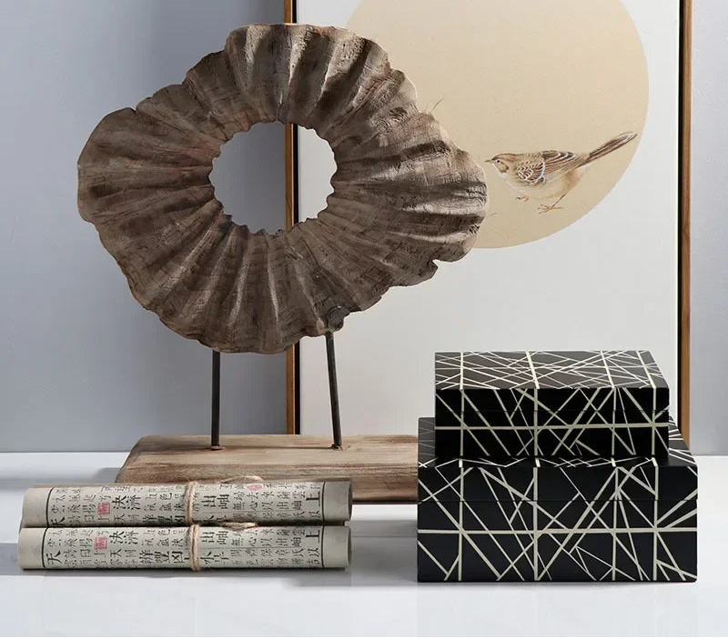 Decorative items including a shell sculpture, books, and a geometric box on a white surface with a painting in the background.