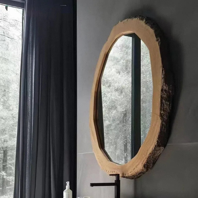 Oval mirror with wooden frame on a gray wall next to a window with dark curtains.