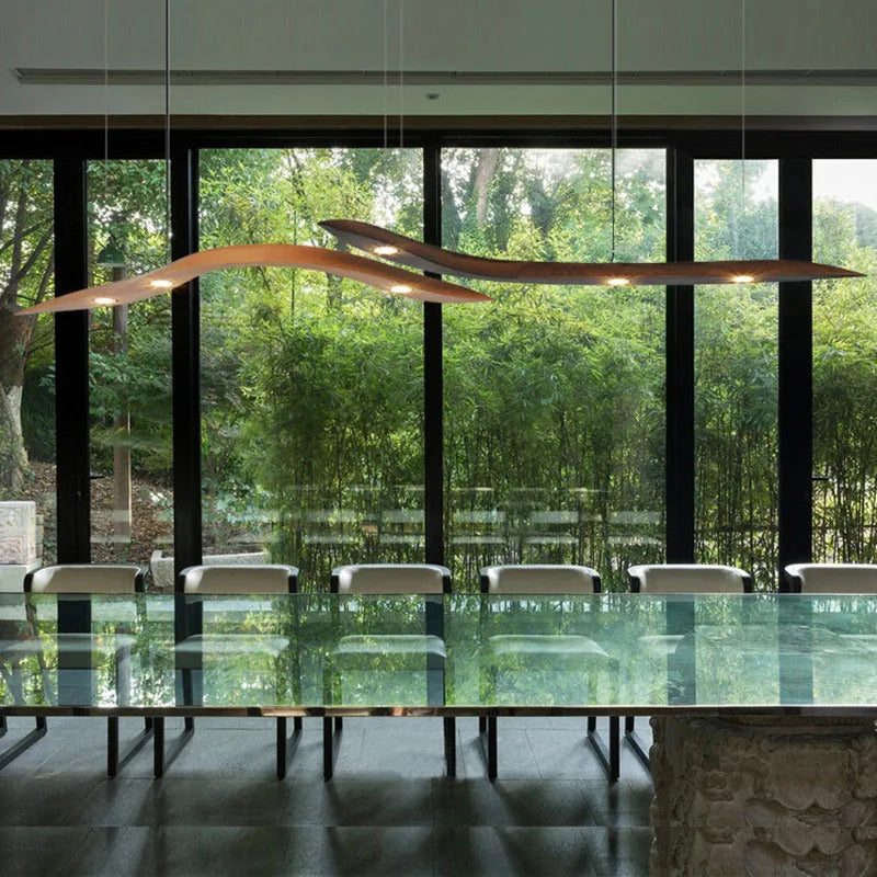 Modern dining room with a long glass table and chairs, large windows, and a decorative ceiling light.