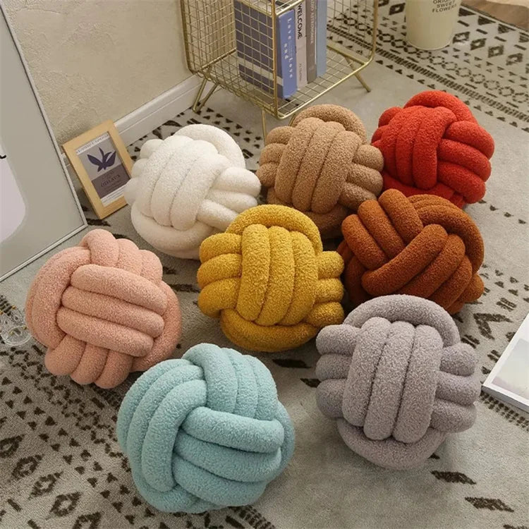 Decorative knot pillows in various colors on a patterned rug.