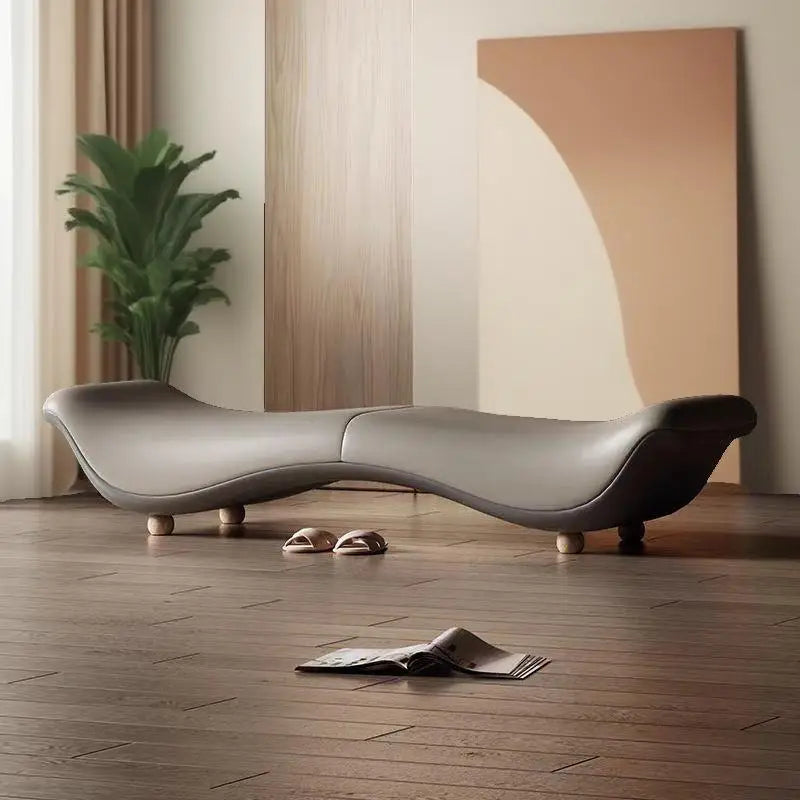 Modern, curved gray sofa in a room with wooden flooring and a plant.