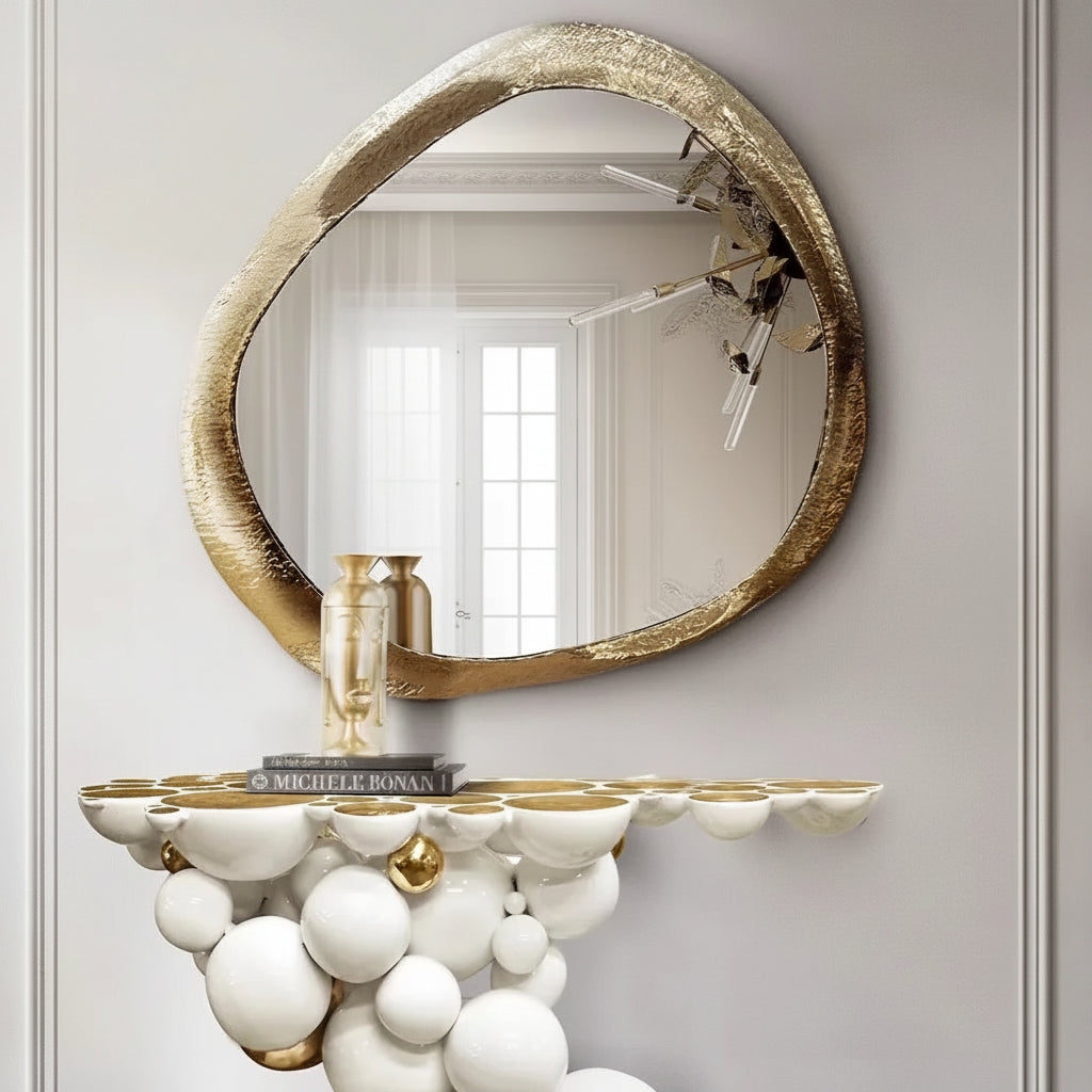 Decorative wall mirror with gold frame and white spherical console table against a gray wall.