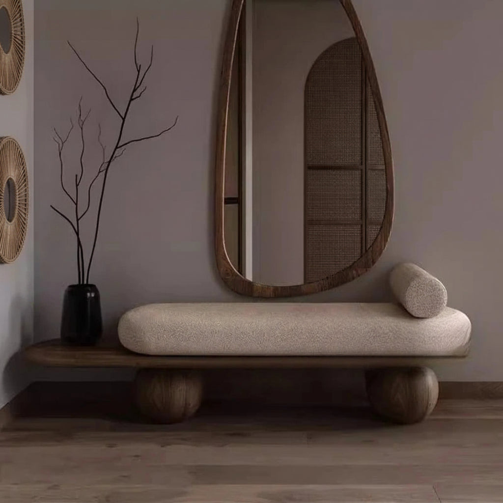 Decorative bench with cushion, vase with branches, and hanging mirror in a room.