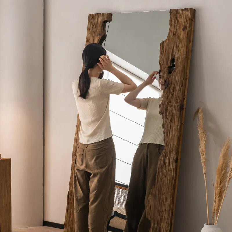 Person adjusting hair in front of a large wooden-framed mirror.