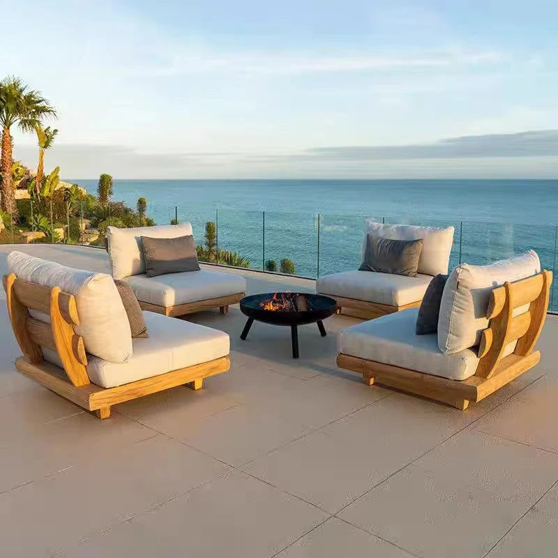 Outdoor patio set with wooden frames and white cushions on a deck overlooking the ocean.