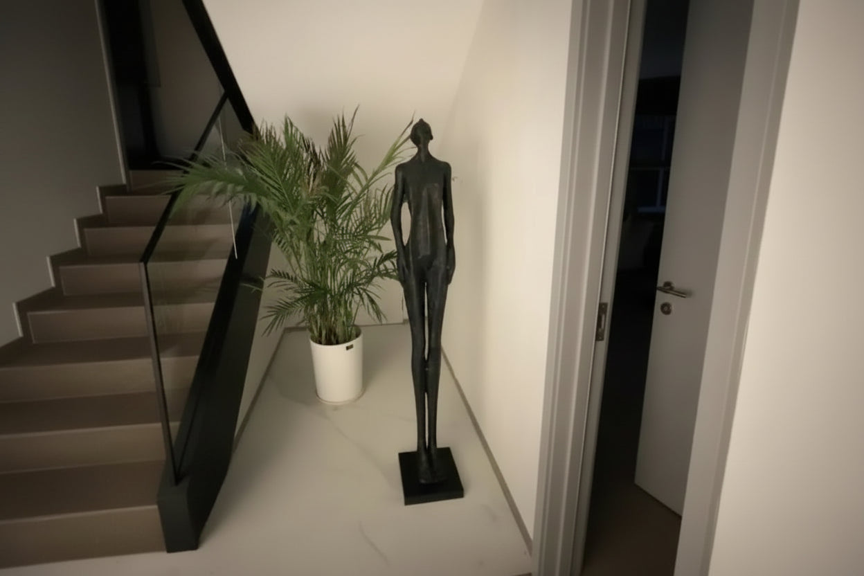 Black abstract sculpture next to a potted plant on a white floor.