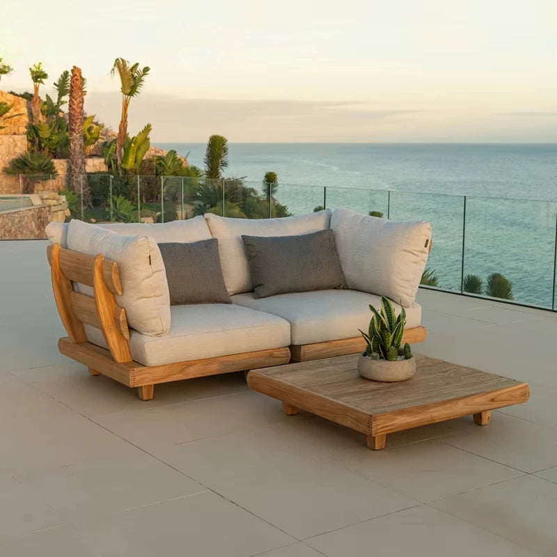 Outdoor patio set with wooden frame and beige cushions on a patio with ocean view.