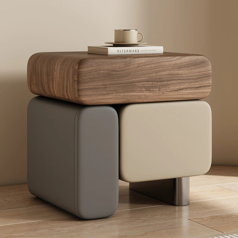 Wooden side table with a beige cushion on a wooden floor against a beige wall.