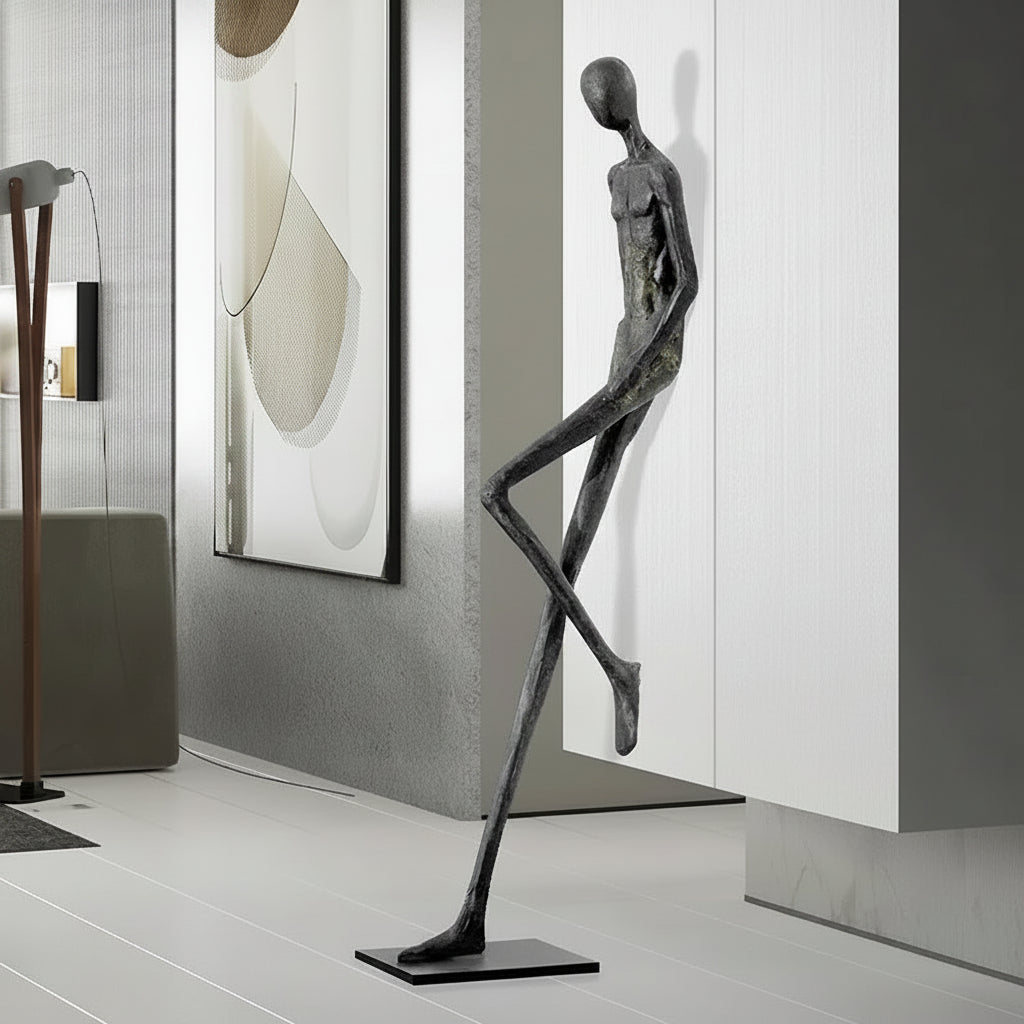 Modern sculpture of a humanoid figure in a minimalistic interior setting with abstract art on the wall.
