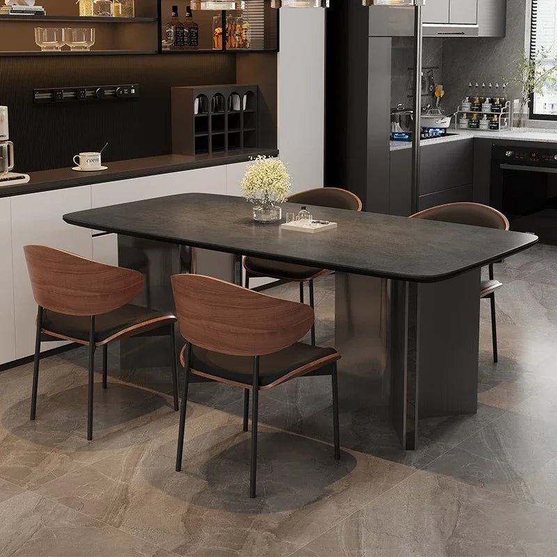 A modern dining table set in a contemporary kitchen. The table has a dark gray stone-look top and a matte dark gray metal pedestal base, surrounded by four chairs with brown wood-look seats and backs and black metal legs.